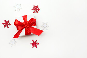 Fototapeta na wymiar Christmas gift box with red ribbon on a white background with shining snowflakes. Flat lay. Copyspace