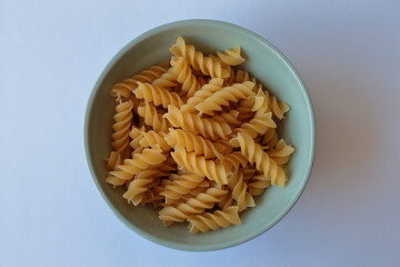 Raw fusilli pasta in a ceramic green plate on a white table. Top view.