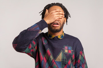 Angry shocked african guy with beard and dreadlocks closing eyes with hand, hiding, dont want to...