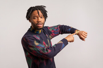 Anxious nervous african man with dreadlocks and beard pointing finger on his wristwatch,...