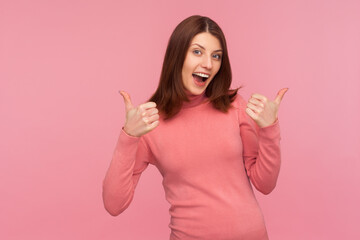 Well done! Extremely happy excited brunette woman showing thumbs up, like gesture, looking at camera with satisfied expression. Indoor studio shot isolated on pink background