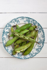 Top down view of raw broadbeans on a white and green plate on a white backdrop horizontal