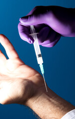 doctor puts injection, syringe and purple glove, blue background