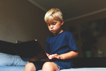 child does homework , lying in bed using his laptop or skyping.
