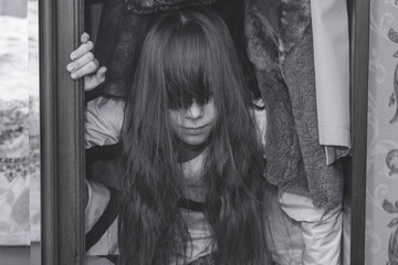 Mad scary girl in cupboard at dark night. Horror background with child possessed by devil. Demon...