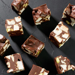 Dessert Rocky road with marshmallows, pistachios, chocolate, cookies, nuts on a black stone background