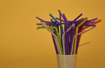 bunch of colorful plastic single-used drinking straws on yellow background copy space