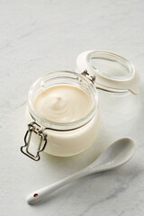 homemade yogurt from farm milk in a glass jar on a light marble background with a ceramic spoon