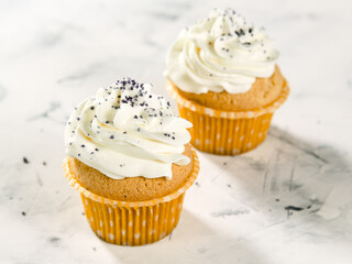 muffin, cupcake with vanilla cream cheese cream and sprinkles on a light marble background