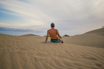 Young man sitting in the desert dunes looking at the horizon.