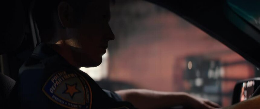 CU Portrait of police officer talking on CB radio while driving in a vehicle through city streets at night. Shot on RED Dragon with 2x Anamorphic lens