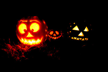Three Halloween pumpkins glowing in the night.