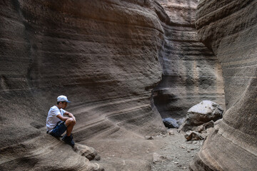 Naklejka premium Young man sitting on some smooth and colorful volcanic stones, Tobas de Colores, Barranco de las Vacas.