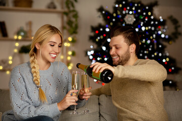 Young couple drinking champagne, celebrating New Year together at home