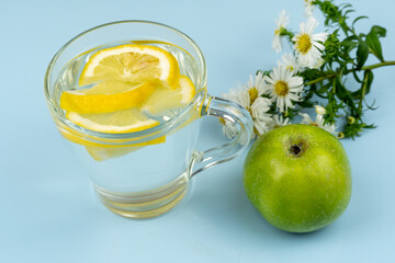 Glass cup with water and lemon slices, green apple and chamomile
