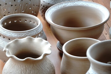handmade unbacked crockery and pots on the table in the potter's studio. clay before firing in a...