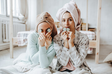 Obraz na płótnie Canvas Two girls make homemade face and hair beauty masks. Cucumbers for the freshness of the skin around the eyes. Women take care of youthful skin