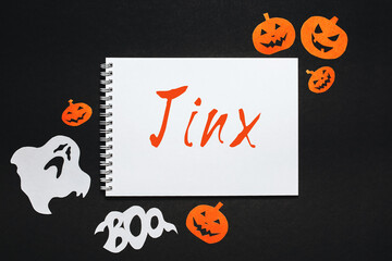 Happy halloween holiday concept. Notepad with text Jinx on black and orange background with bats, pumpkins and ghosts