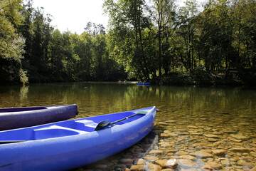 canoes or kayaks on the bank of a beautiful river with a background of trees and kayaks descending...