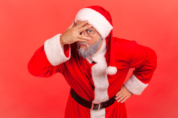 Portrait of curious nosy man in santa claus costume pretending to close eyes with hand attentively...