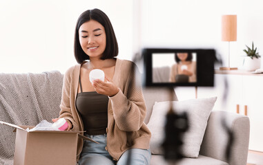 Happy asian woman filming product review for beauty blog