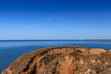 A man standing on a sandy rock and looking at the sea.