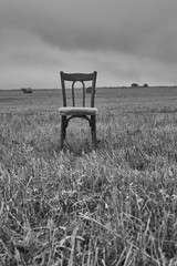 One old chair stands in a mown field against a cloudy sky.