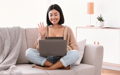 Happy woman using laptop for video call and waving