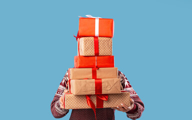 Young woman holding stack of gift boxes over blue studio background