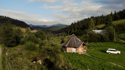 Hut and car near the forest. An old house against the sky and mountains visible in the distance.