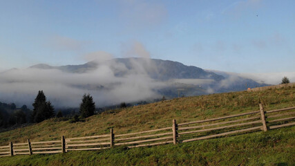 Wooden fence near mountain village. Lovely foggy day in mountains.