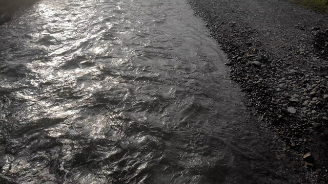 Shiny mountain river. Wet pebbles and boulders on the beach near the water.