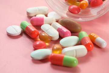 Close up of many colorful pills and capsules spilling on pink background 