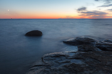 Twilight sunset over rocky shore of Baltic sea. Almost clear sky and orange strap along the horison. Estonia.