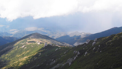 The bright sun illuminates green mountain hills. White cloud of fog is high above the mountains.