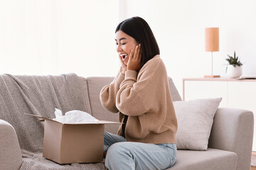 Excited asian lady unpacking parcel after online shopping
