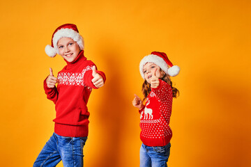 Happy children in red sweaters with deer having fun and showing thumbs up on Christmas day against yellow background