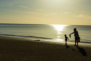 Asian boy and mother stand on the sandy beach and look at the sea.