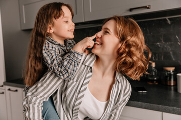 Close-up portrait of curly-haired young mom and her little cheerful daughter in kitchen