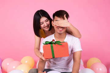 Couple in love.Asain woman surprising his boyfriend with a gift. Young woman on birthday holiday party. Celebrating with pastel color balloon.