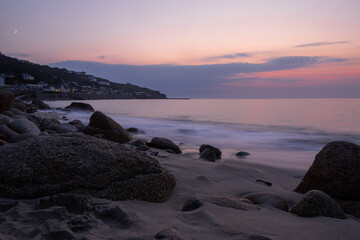 Rocks on the beach at sunset with town in background