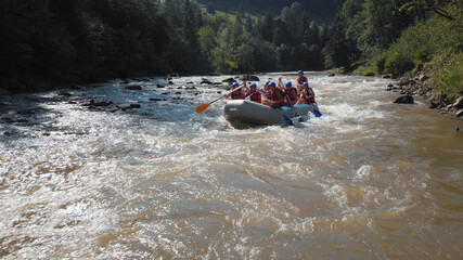 Rafting boat on the fast mountain river. Group of tourists in helmets and life vests in white boat....