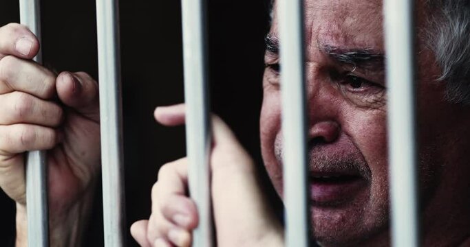 Desperate old man behind bars. Imprisoned person