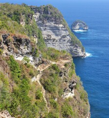 Fototapeta premium Steep cliff with rocky coastline, natural arch in background on Nusa Penida, Bali, Indonesia