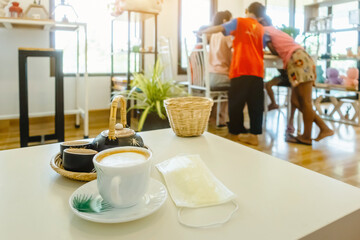 Hot Cappuccino coffee with protective mask on a wooden table for people being quarantined in the situation of the spread of the corona virus (Covid-19).  New normal lifestyle concept. Selective focus