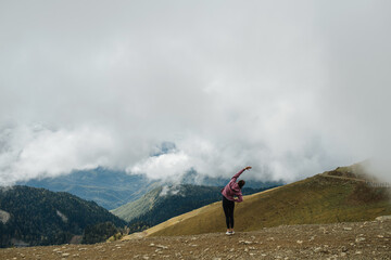 Long shot of a woman doing side bends, exercising high up in cloudy mountains.