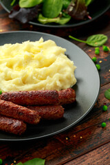 Vegetarian vegan sausages with mashed potato and green peas in black plate
