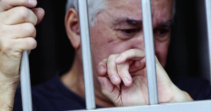 Desperate old man behind bars. Imprisoned person