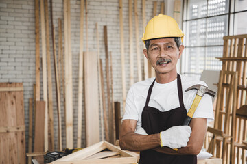 A senior carpenter holding hammer for creating house wooden interior accessories via laptop in the further refinement within a building or condominium. Construction learning concept.
