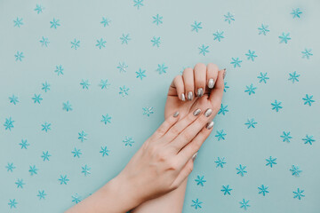 Female hands with silver manicure on blue background with snowflakes.